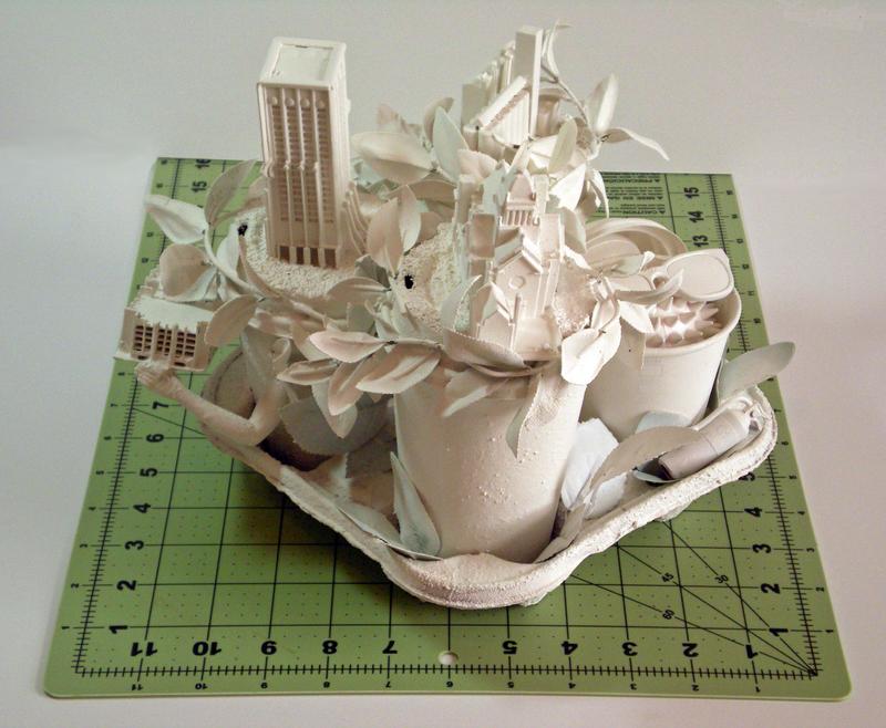 Disposable tray with coffee cups and found objects like doll arms, spiky ball wearing doll sunglasses resembling the COVID-19 virus and city buildings made from scratch by artist.