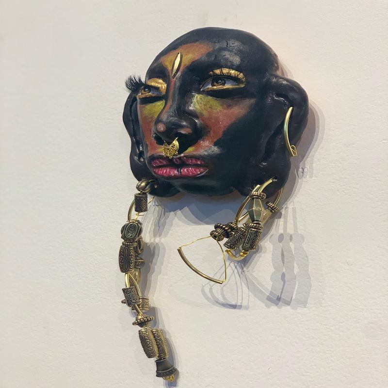 A sculpture of a Black womans face. The texture is smooth from the acrylic paint. The back of the sculpture is flat. 