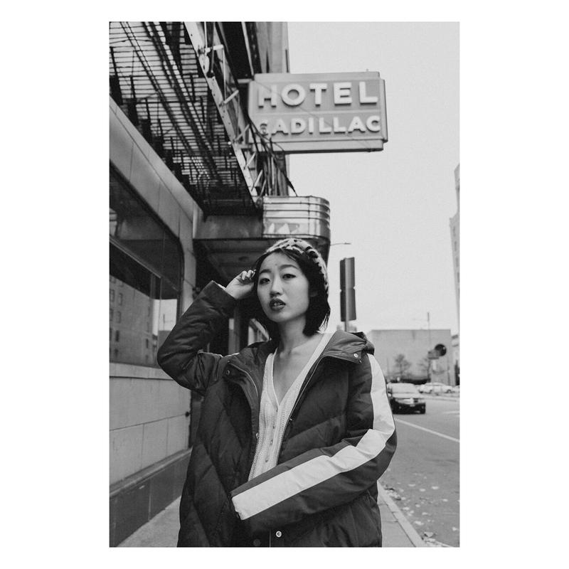 Black and white photograph of a girl wearing a winter coat and a beret in front of an old hotel called Hotel Cadilllac.